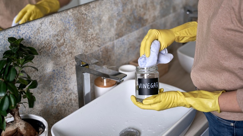 Woman dampening cloth with vinegar to clean bathroom