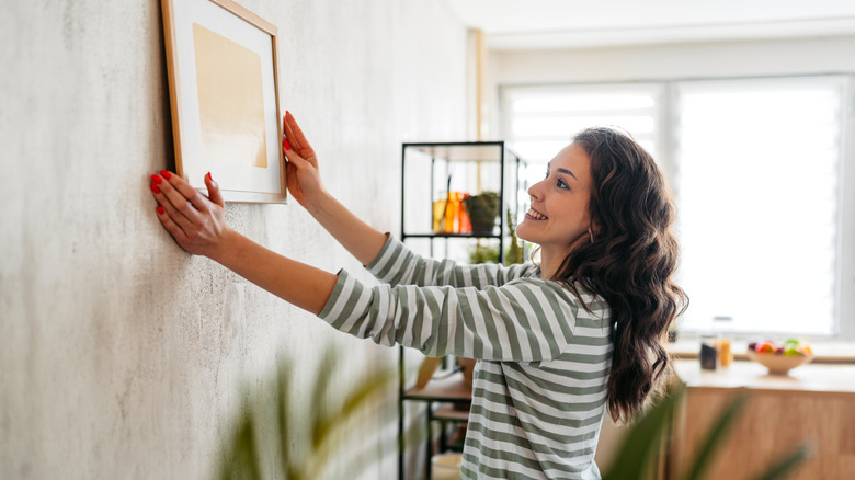 Dark-haired woman hanging a picture on a wall as if planning the start of a gallery wall