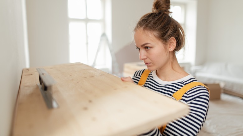 woman mounting shelf on wall