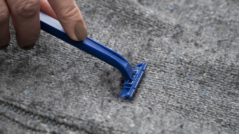 A woman shaving off fabric pills on a sweater with a disposable razor