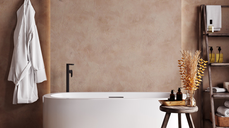 Bathroom featuring a bathtub, bathrobe, fixture, with brown texture walls behind it