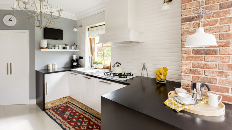 black countertops in a small kitchen with white cabinet doors and whitewashed brick walls