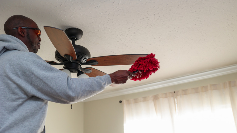 Person cleaning a ceiling fan with a duster