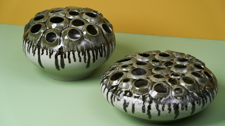 Two ceramic flower frogs on a sage surface.