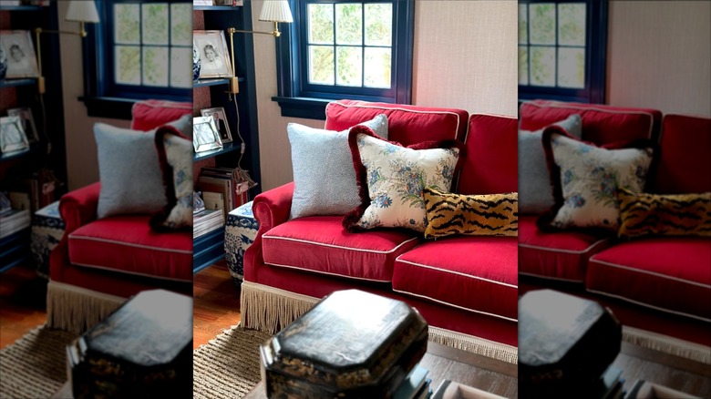 Bold red sofa with white piping, taupe fringe, and decorated with patterned throw pillows