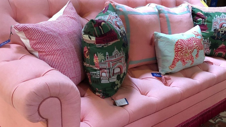 A pink sofa with piping and fringe on the bottom paired with patterned pillows with tassels