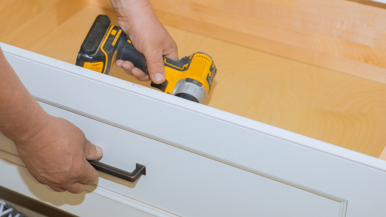 Man's hands screwing a handle in a drawer side.