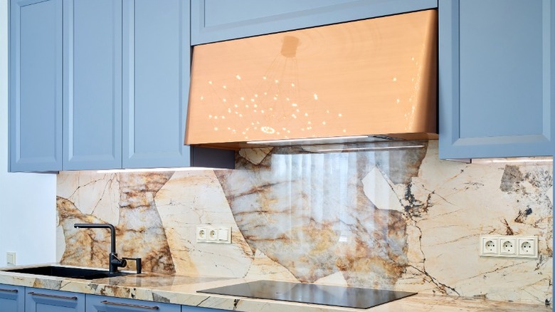 copper kitchen hood surrounded by light blue cabinets over marble counter and backsplash
