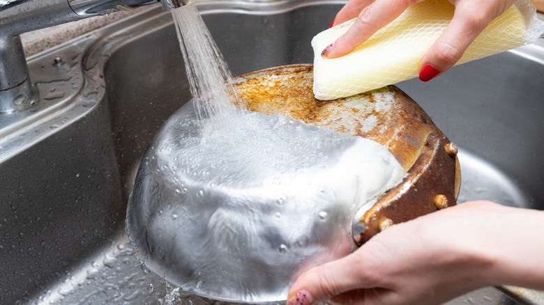 person cleaning bottom of burnt pan