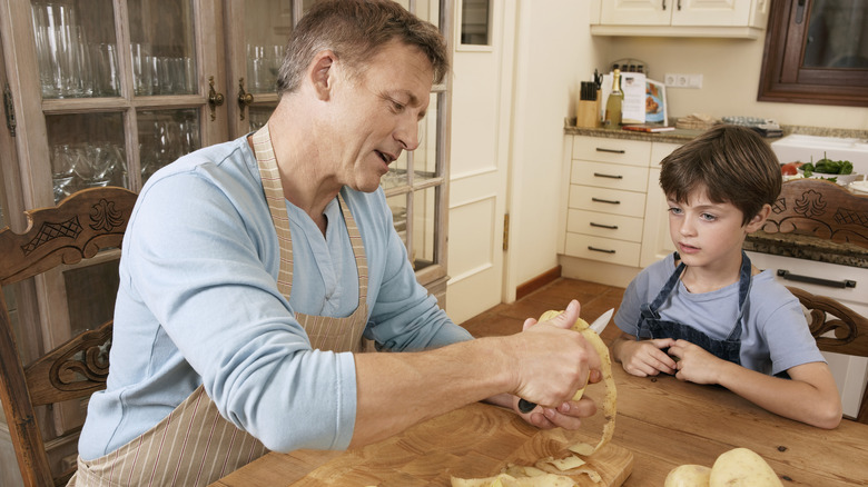 Man showing son how to peel potatoes