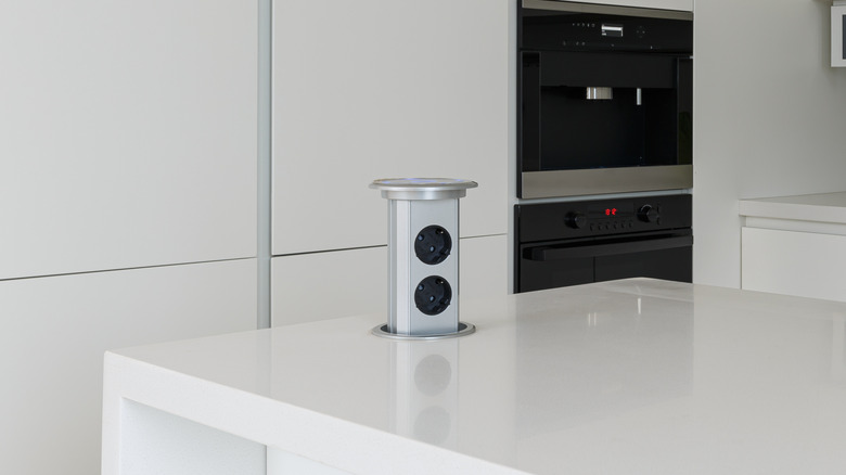 A white kitchen with a pop up outlet installed on the countertop