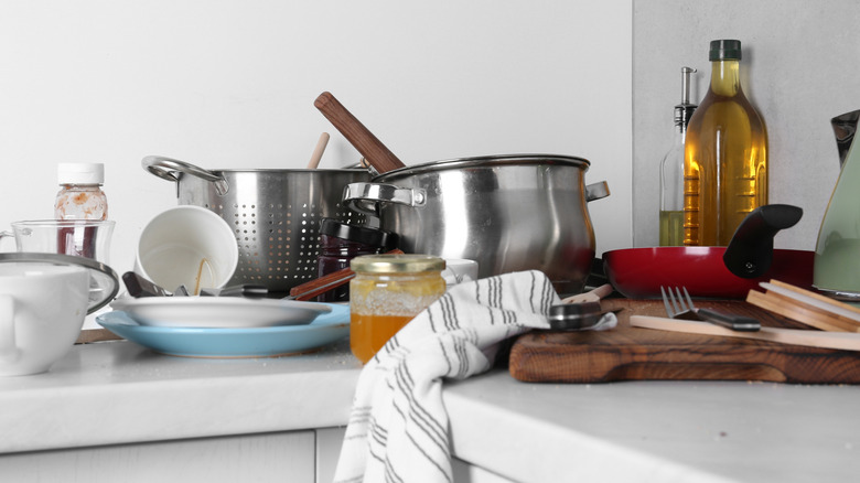 A messy kitchen countertop covered with pots, pans, and other kitchen items