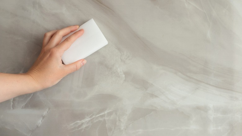 A person uses a melamine sponge on a smooth surface
