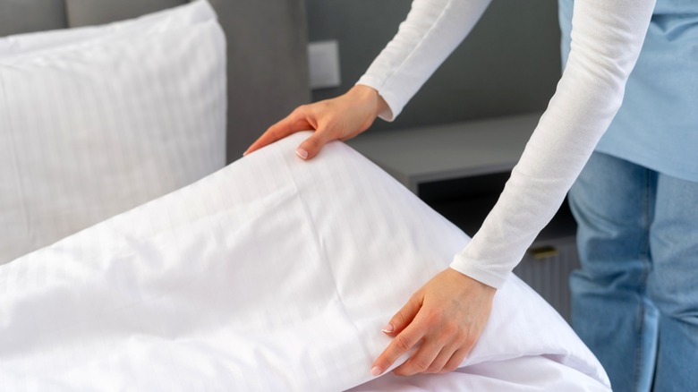 person tidying white comforter on bed