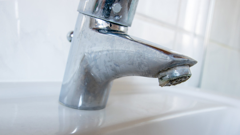 Close-up of a bathroom faucet coated with chalky white limescale film