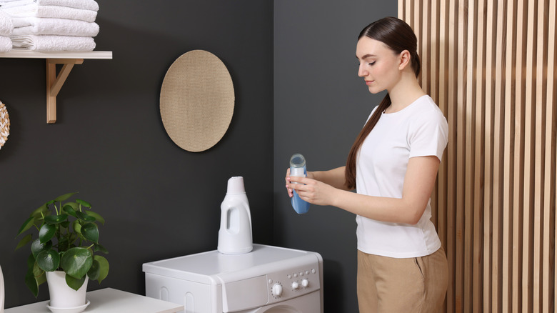 A woman pouring fabric softener into a cap in the laundry room