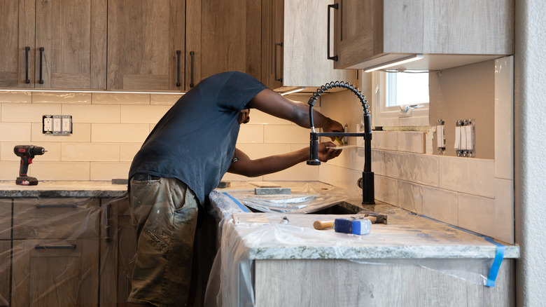 An African American man pieces together tiles for a kitchen backsplash.