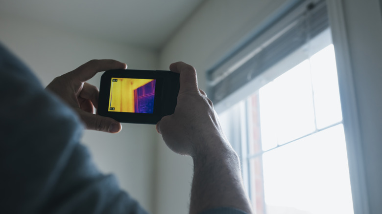 A person holds their thermal camera up to the windowsill to analyze the temperature