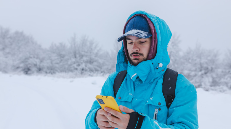 A man outside in the snow wearing lots of winter clothing looks at his phone