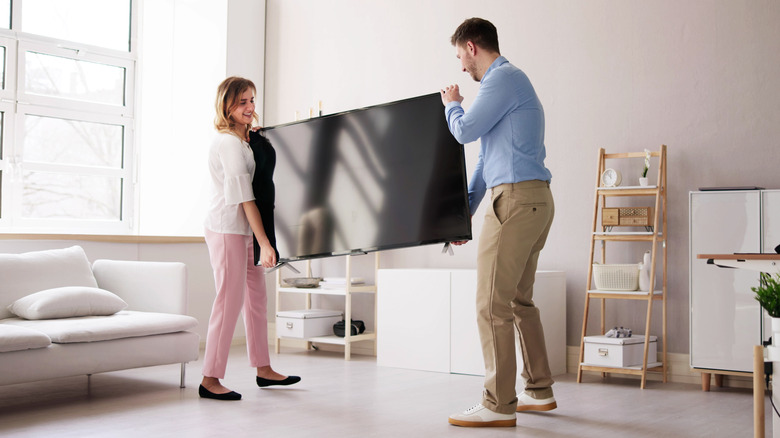 Couple moving TV in home.