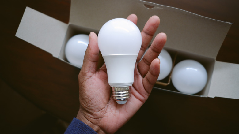 A hand is holding an LED light bulb pulled from a box.