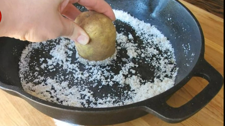 Person cleaning cast iron pan with potato and salt