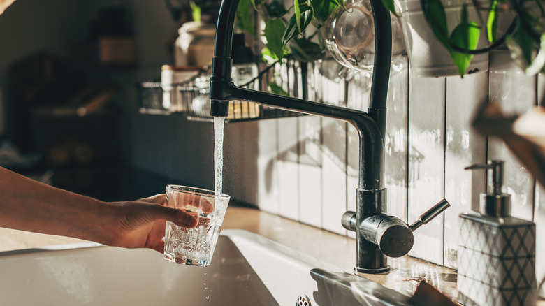 Person pouring a glass of water from kitchen faucet