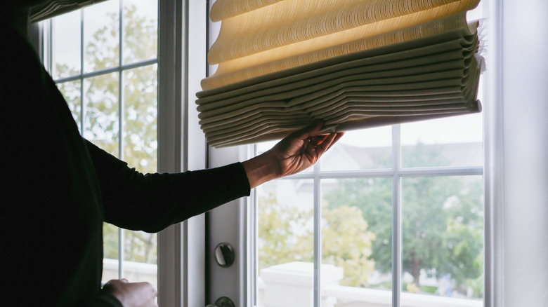 A person closing Roman shades on a door with windows