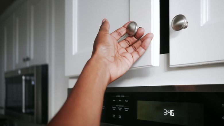 A person touches a cabinet pull to open a cabinet door