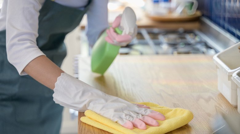 A woman wearing cleaning gloves sprays and wipes down her kitchen counter