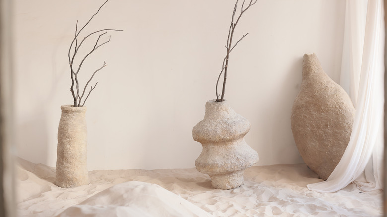 three textured vases in sand with a white curtain