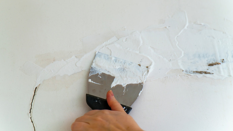 Ha hand using a putty knife to fix a crack in a wall