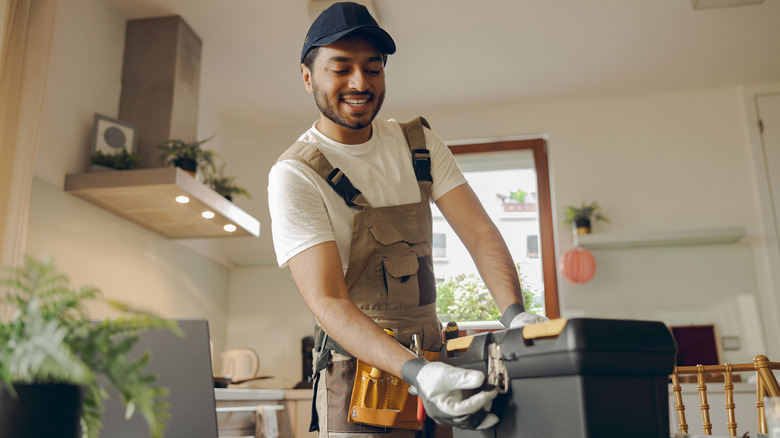 Man in handy-man gear and gloves opening a toolbox in a modern kitchen
