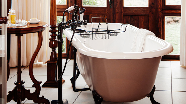 A luxury colonial contemporary bathroom with a vintage ceramic bathtub and dark wood accents
