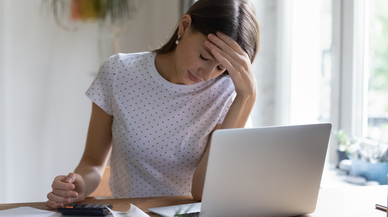 Woman at computer with calculator, looking upset