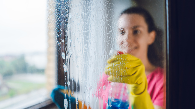 woman in yellow cleaning gloves cleans window at home with glass cleaner
