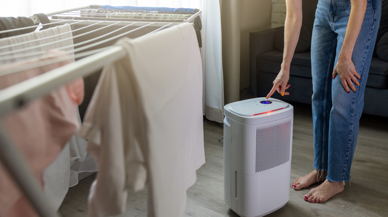 Woman pressing a button on a dehumidifier in a laundry room with clothes hanging on a drying rack