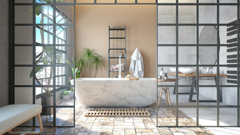 A modern bathroom with khaki walls, a stand alone marble tub, and a tiled rug