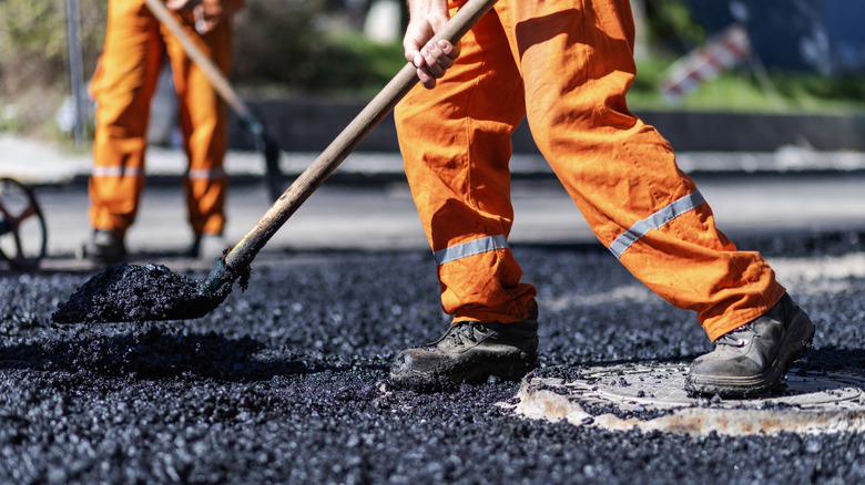 A road worker in an orange jumpsuit standing on fresh asphalt