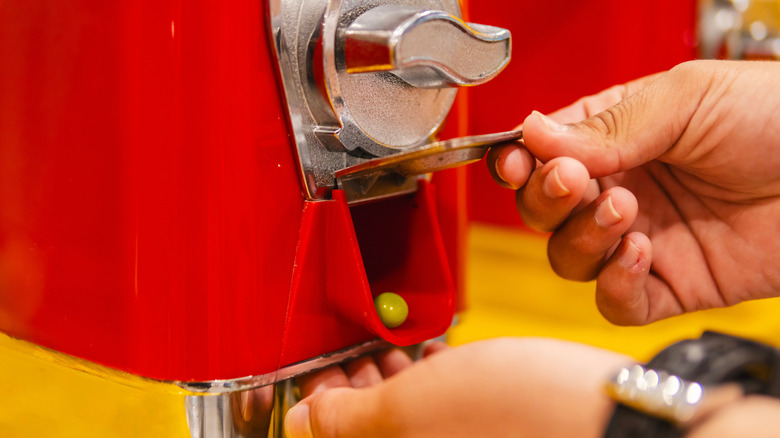 A hand gets a gumball from a machine