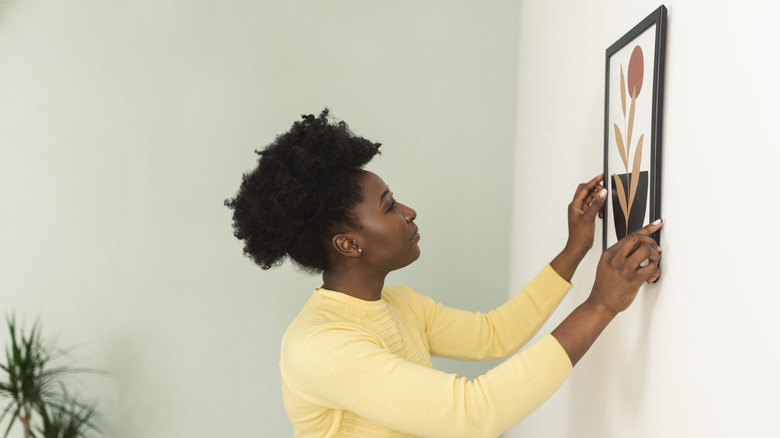 A woman hangs artwork in her bathroom