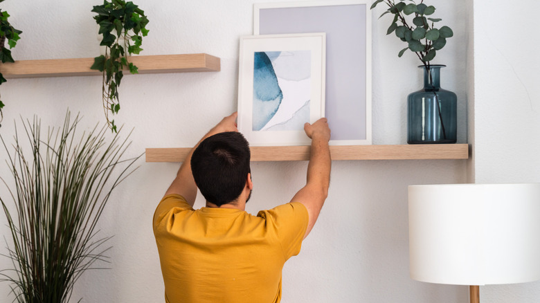 A man in a yellow shirt hanging modern art.