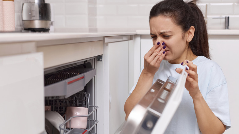 Woman opening dishwasher and reacting to unpleasant smell
