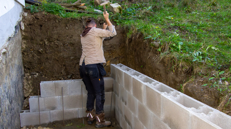Person uses a mallet to compact concrete bricks into place while building a retaining wall over four feet.