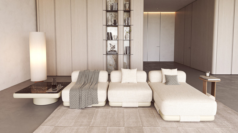 Contemporary living area featuring cream modular seating, soft lighting, a floor lamp, and built in shelving with decorative accents.