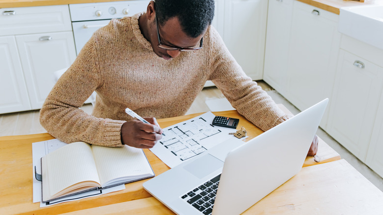 a man sits at kitchen island working on blueprint of home