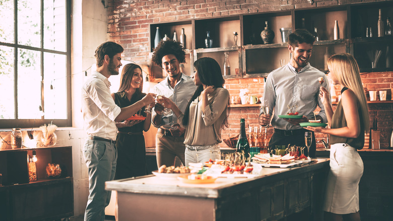 friends enjoying drinks and food gathered around a kitchen island