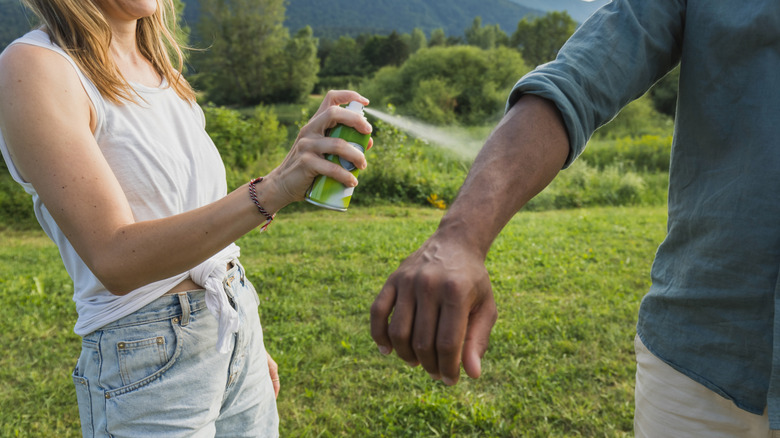 Woman spraying man's arm with bug spray in a field
