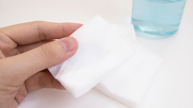 Hand holding cotton square next to bottle of rubbing alcohol