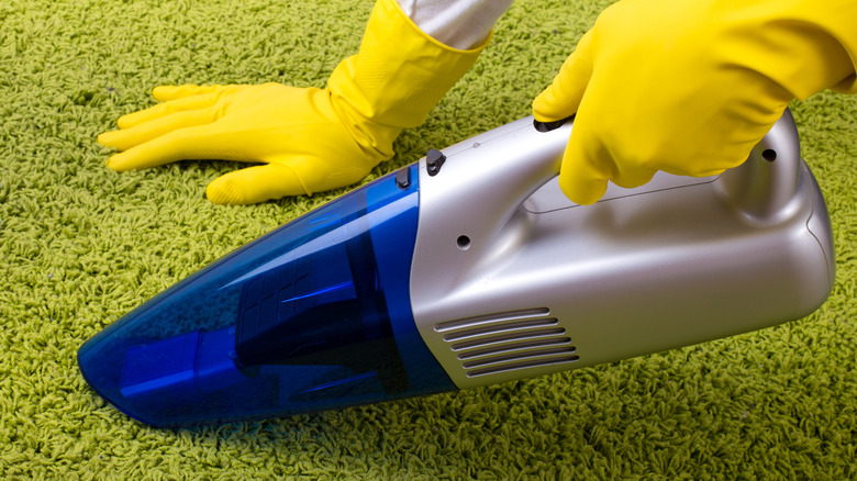 Someone using a handheld vacuum on a green carpet.